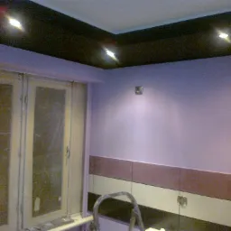 Pomieszczenie po odświeżeniu: ściany pomalowane na liliowo, ciemny sufit z zamontowanymi punktowymi lampami, widoczny fragment okna i drabiny malarskiej.